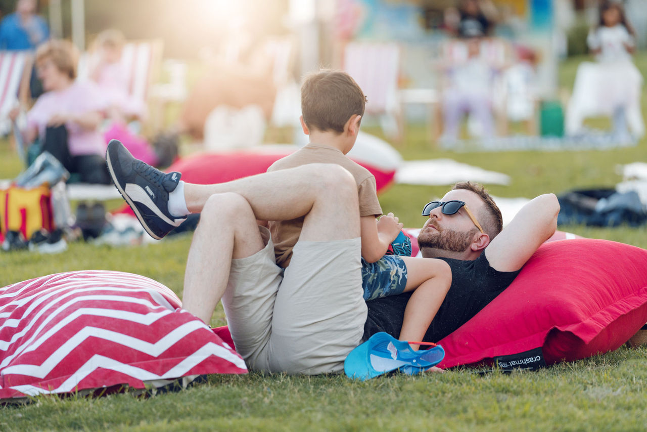 Boy sitting on his father's stomach and chatting at an Outdoor Cinema in the Suburbs event at Victoria Park.