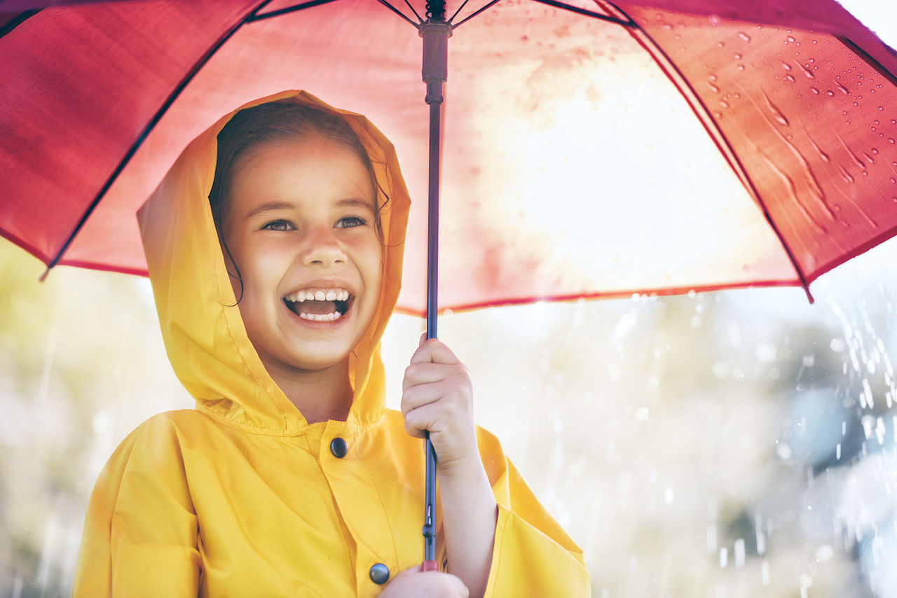 Happy, young girl with a yellow raincoat and red umbrella in the rain.