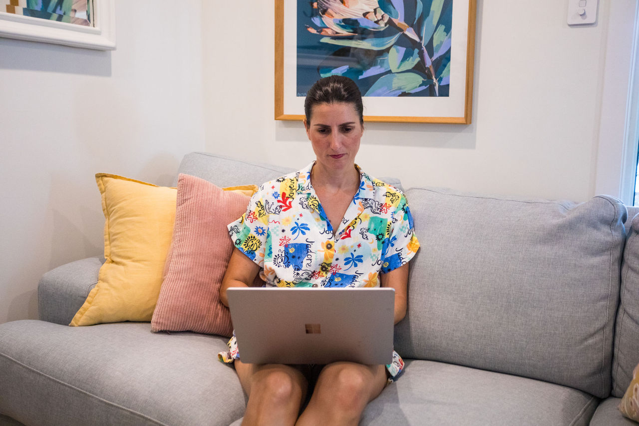 Woman sitting on a couch in a lounge room using a laptop.