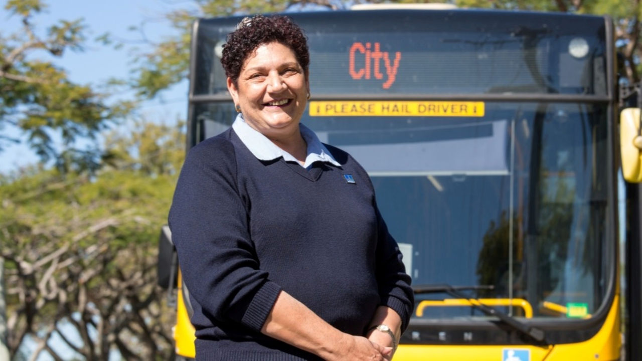 Female bus driver, smiling, with bus in background.