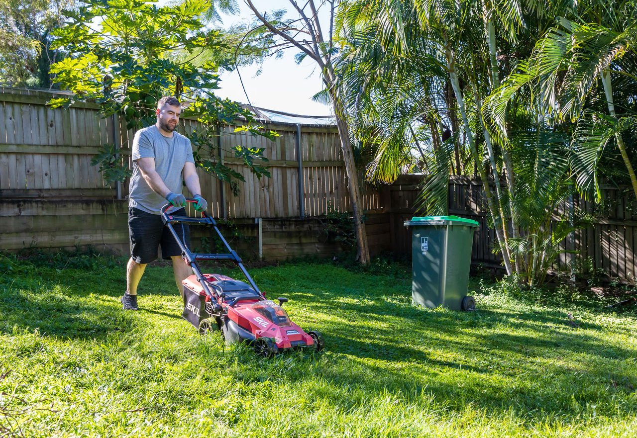 Man pushing a lawnmower in a backyard to cut grass.