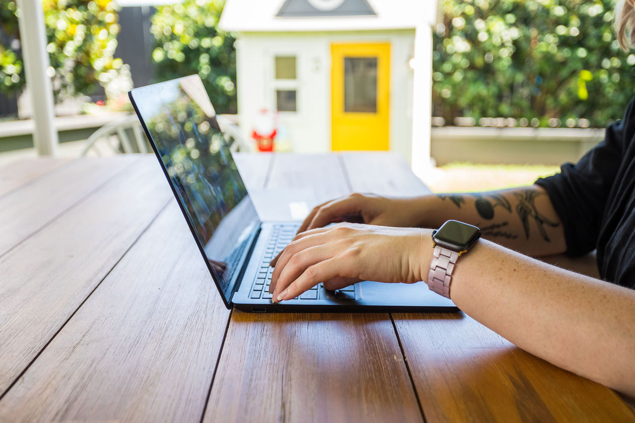 Close-up a woman's hands on a laptop at an outside table.