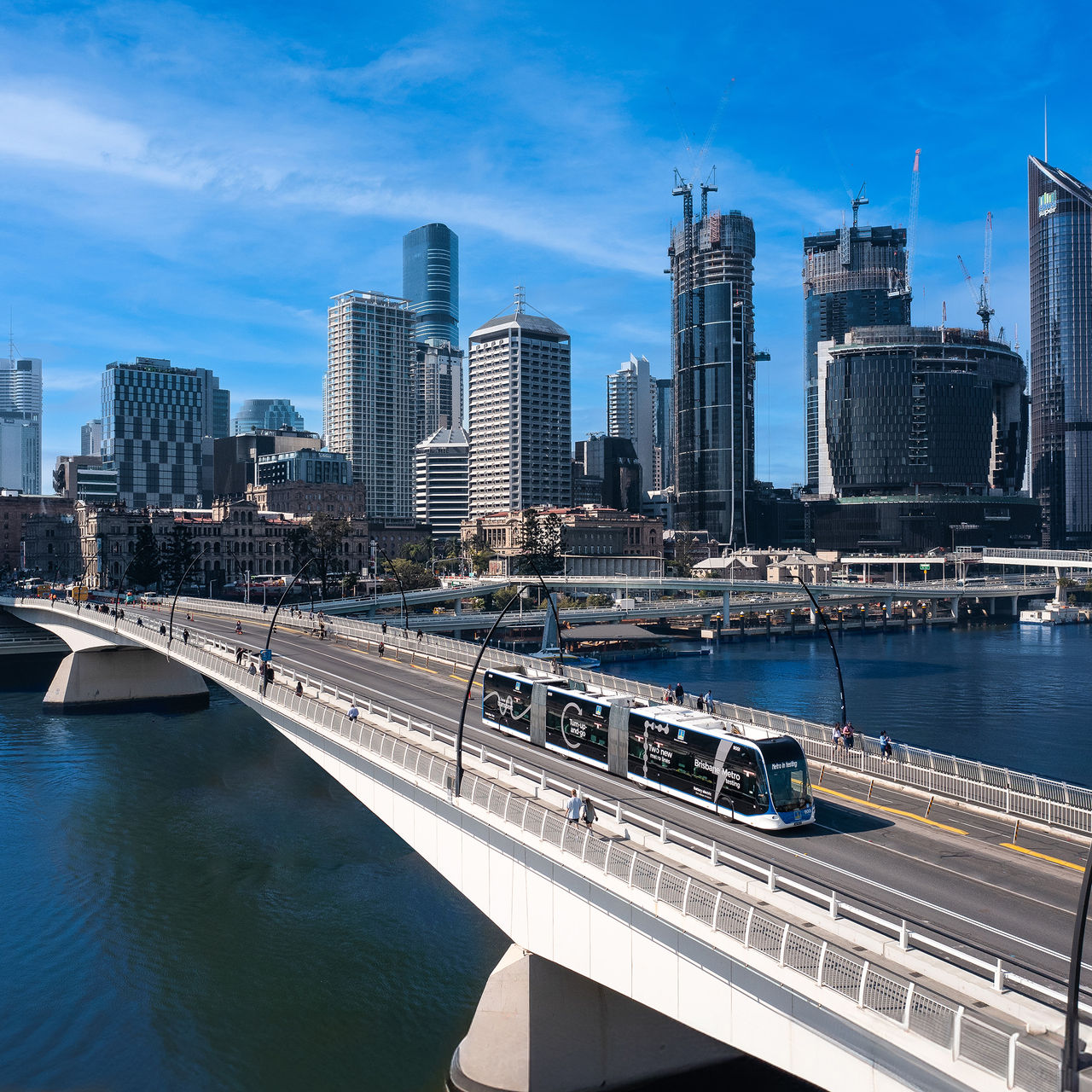 A Brisbane Metro travelling along a bridge with Brisbane City in the background.