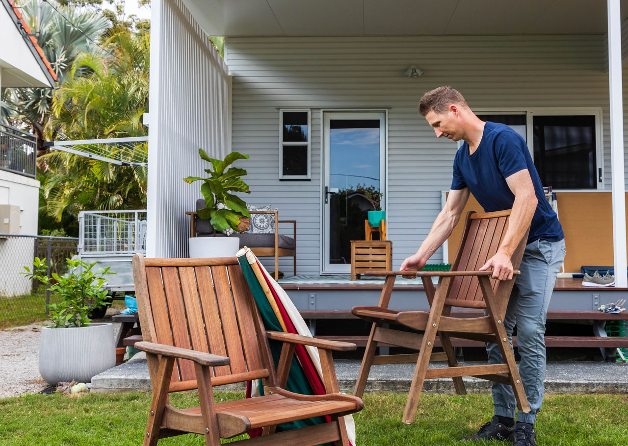 Man packing away wooden outdoor furniture.