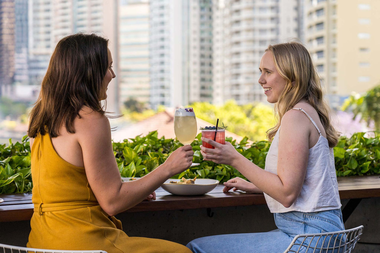 Two women enjoying a drink and meal at Fiume, Howard Smith Wharves. The Brisbane CBD forms the image background.