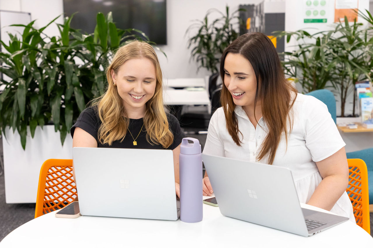 Two women working together. Looking at Surface Pro computer screens in office setting.