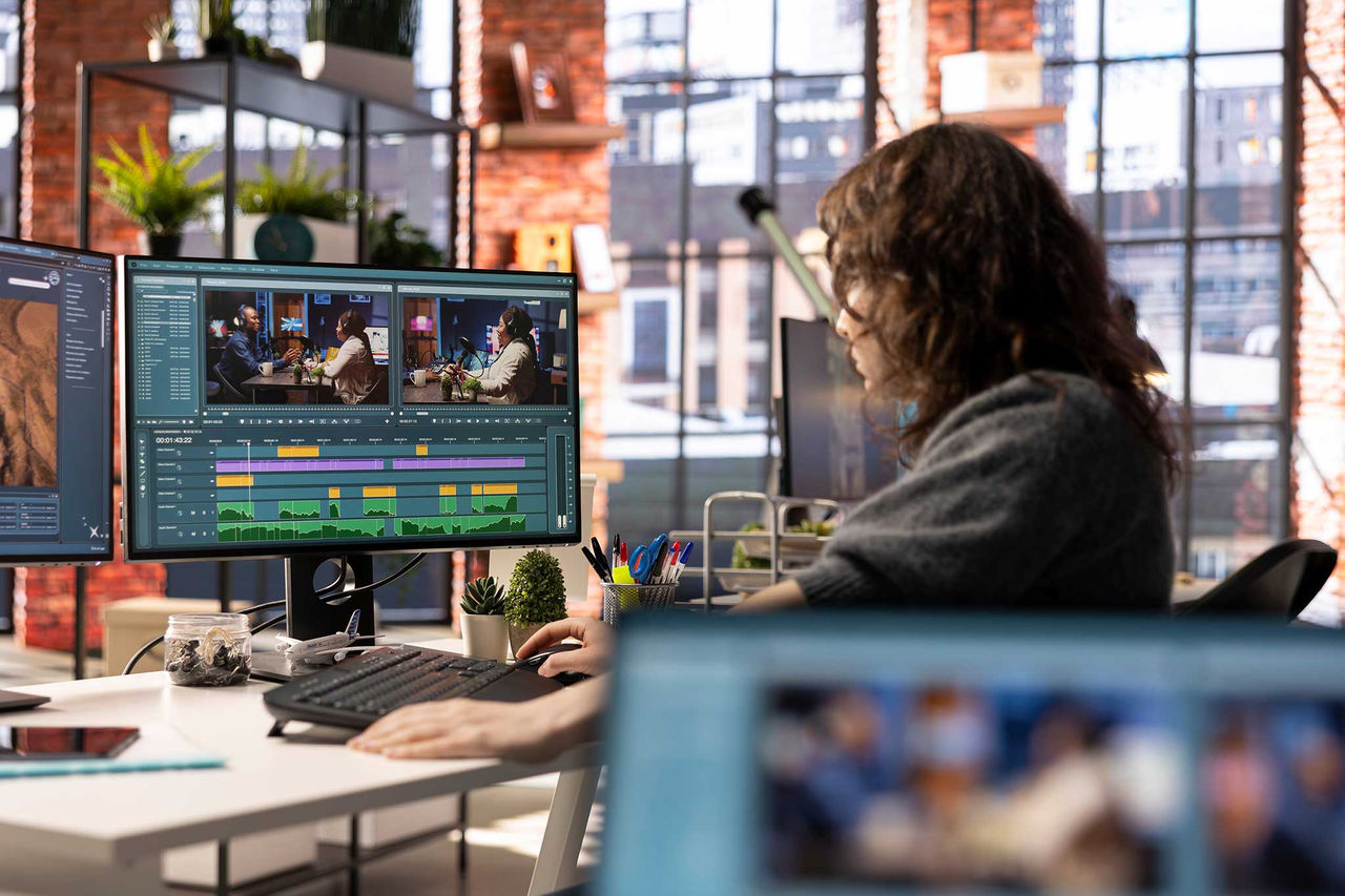 Woman using video editing software on a double-screen computer set-up in an office environment.