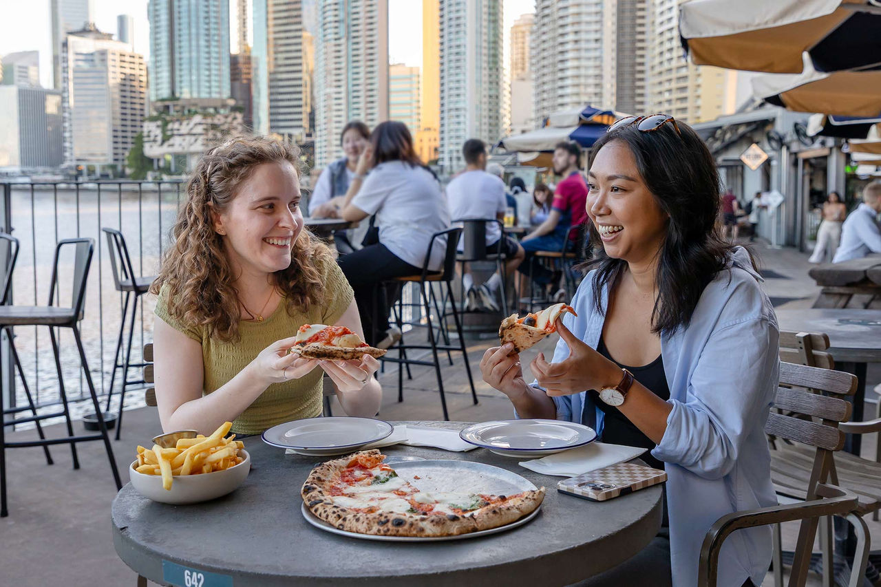 Two young women eating pizza and chips at Howard Smith Wharves.