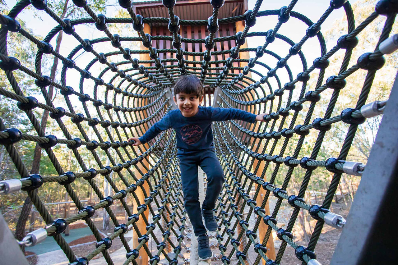 Boy climbing in a black net at Warril Parkland playground.