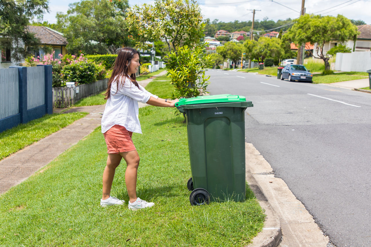 Woman putting her green waste bin on footpath for collection.