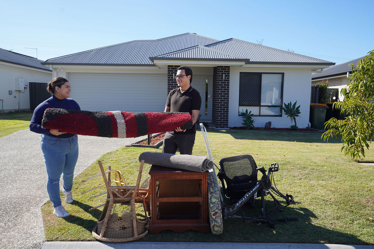 Couple placing items on footpath in front of low set home for kerbside collection.