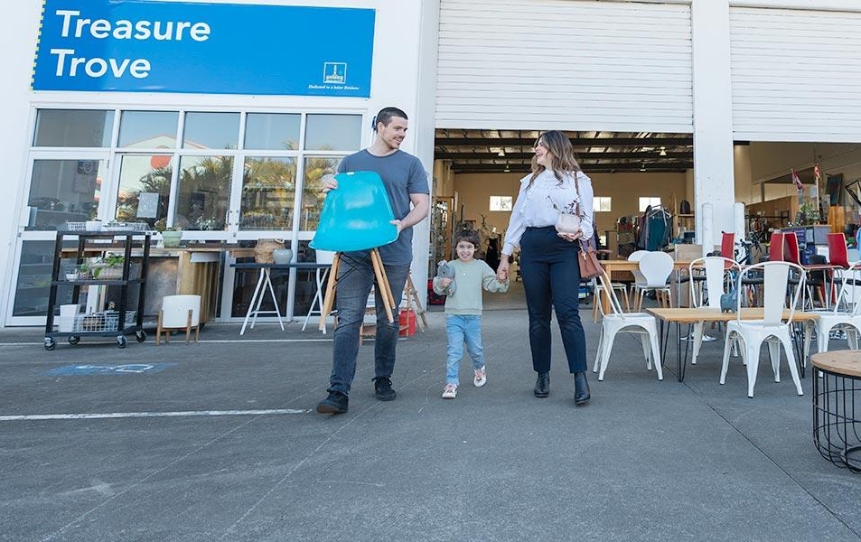 Young family of 3 coming out of a Council Treasure Trove with purchased items including a blue chair in hand.