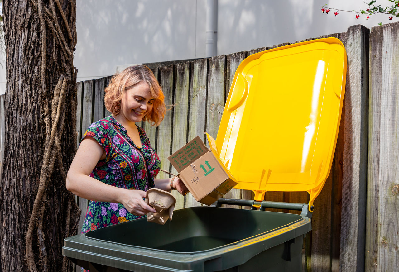 Woman putting recycling waste in yellow bin.
