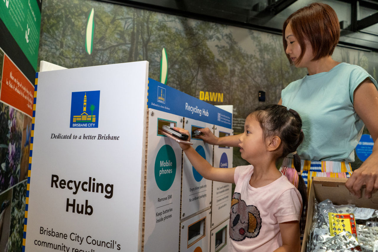 Mother and daughter at a recycling hub placing items for recycling in the appropriate containers.