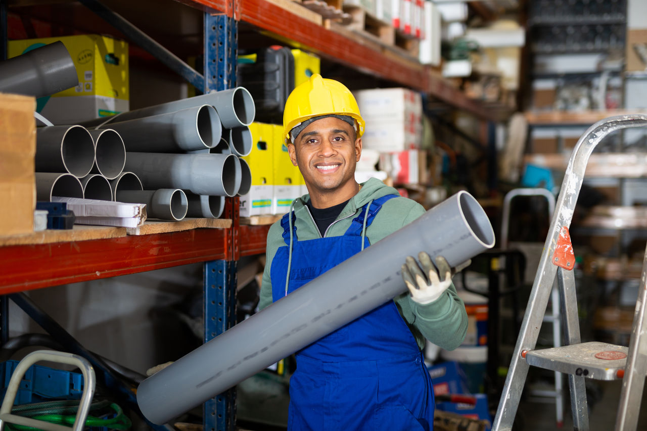 Plumber in protective helmet and overalls selects plastic pipes in a hardware store