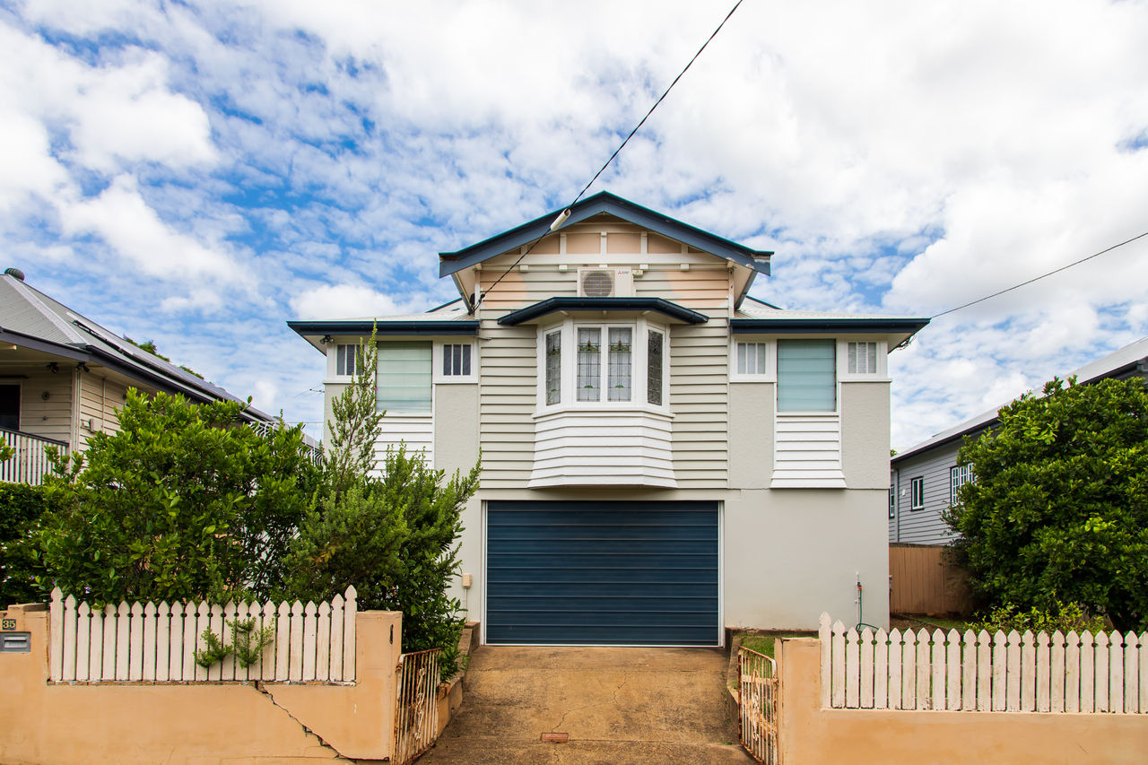 Traditional Brisbane character house with lush green bushes featuring white picket fence, tall windows and attic.