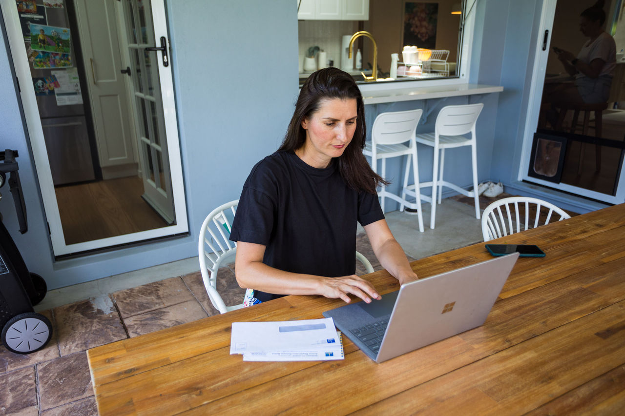 Woman using a computer on an outdoor table with rates notice and envelope beside her.