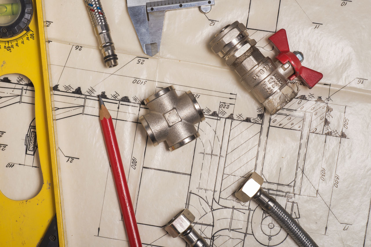 Plumbing parts and fixutes, spirit level and a pencil sitting on top of black and white plumbing plans.