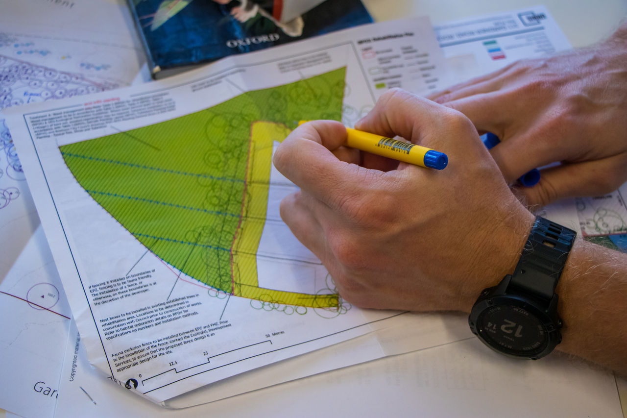 Close-up of a man holding a blue pen marking up a subdivision plan.