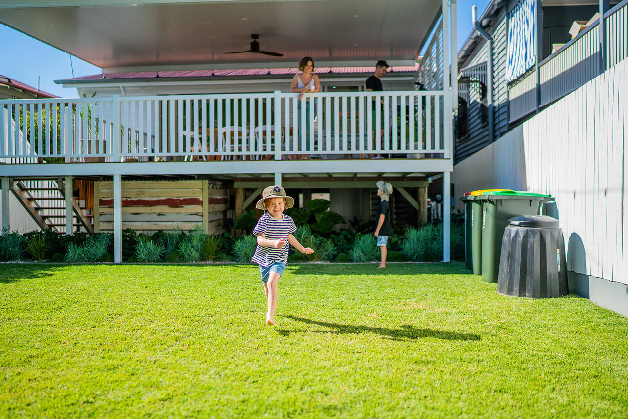 Children in backyard of a character house. Child running towards camera and parents standing on back deck.
