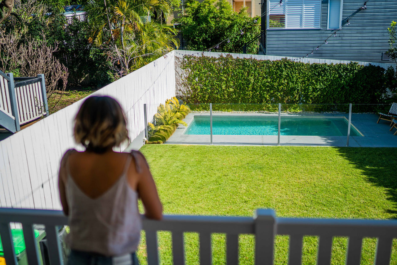 Woman on a backyard deck overlooking lawn and fence swimming pool.