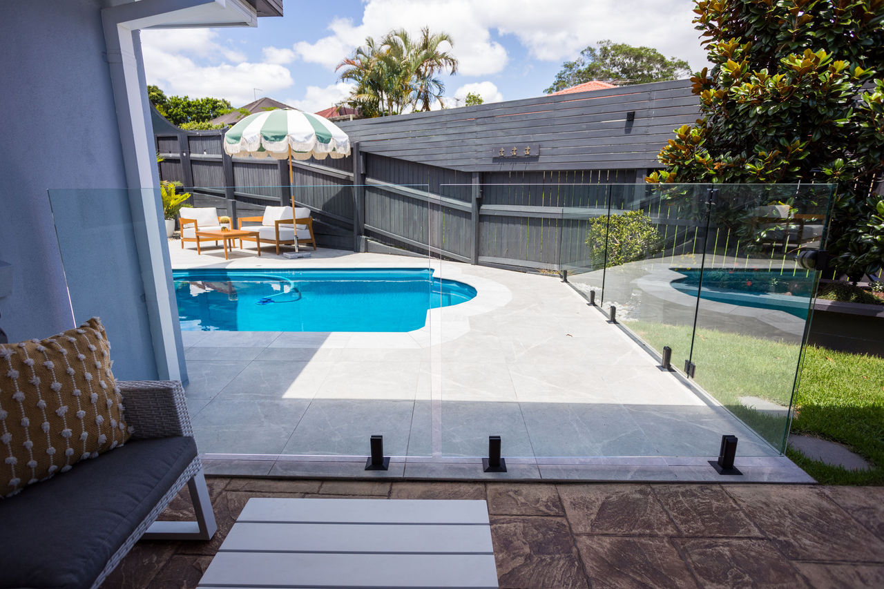 Backyard swimming pool fenced with glass panels.