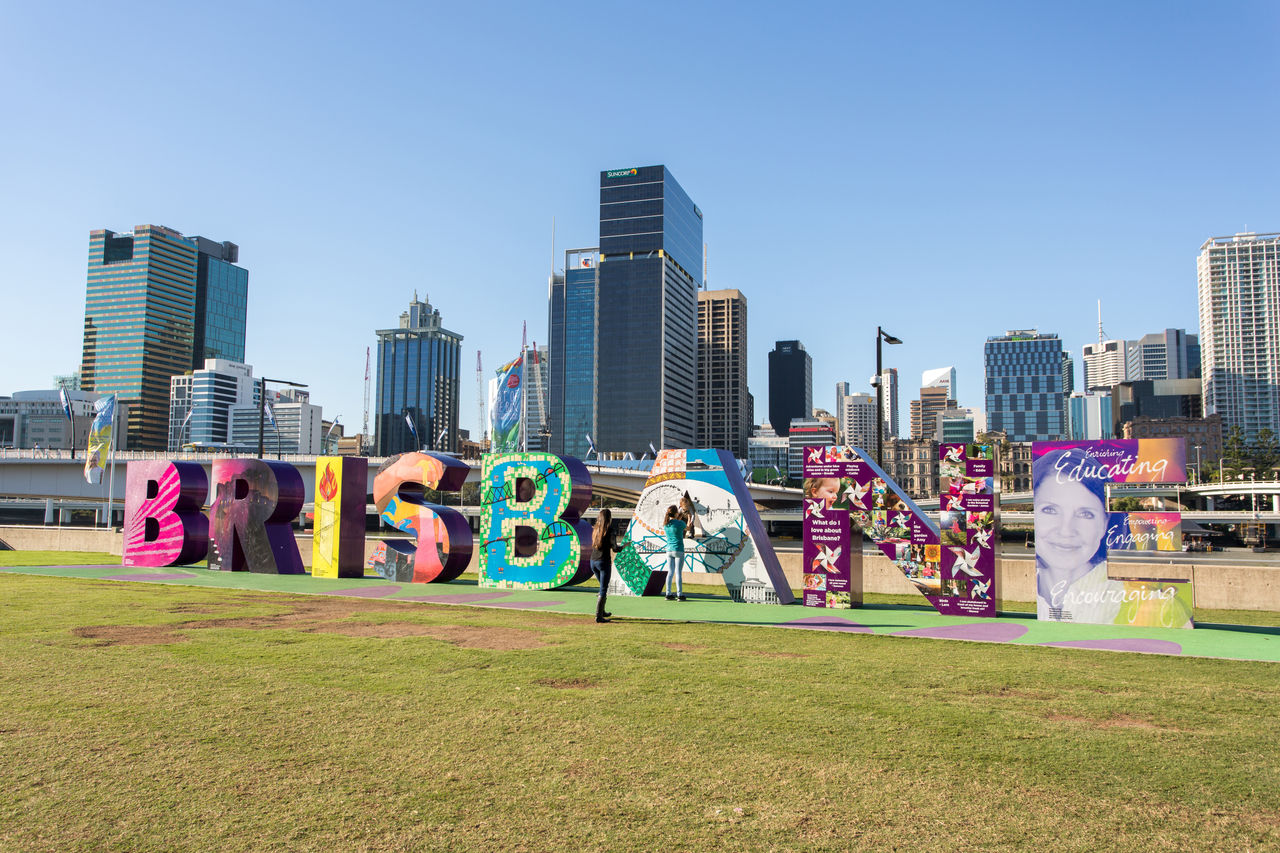 3 children at Brisbane sign at South Bank Parklands with Brisbane CBD in background.