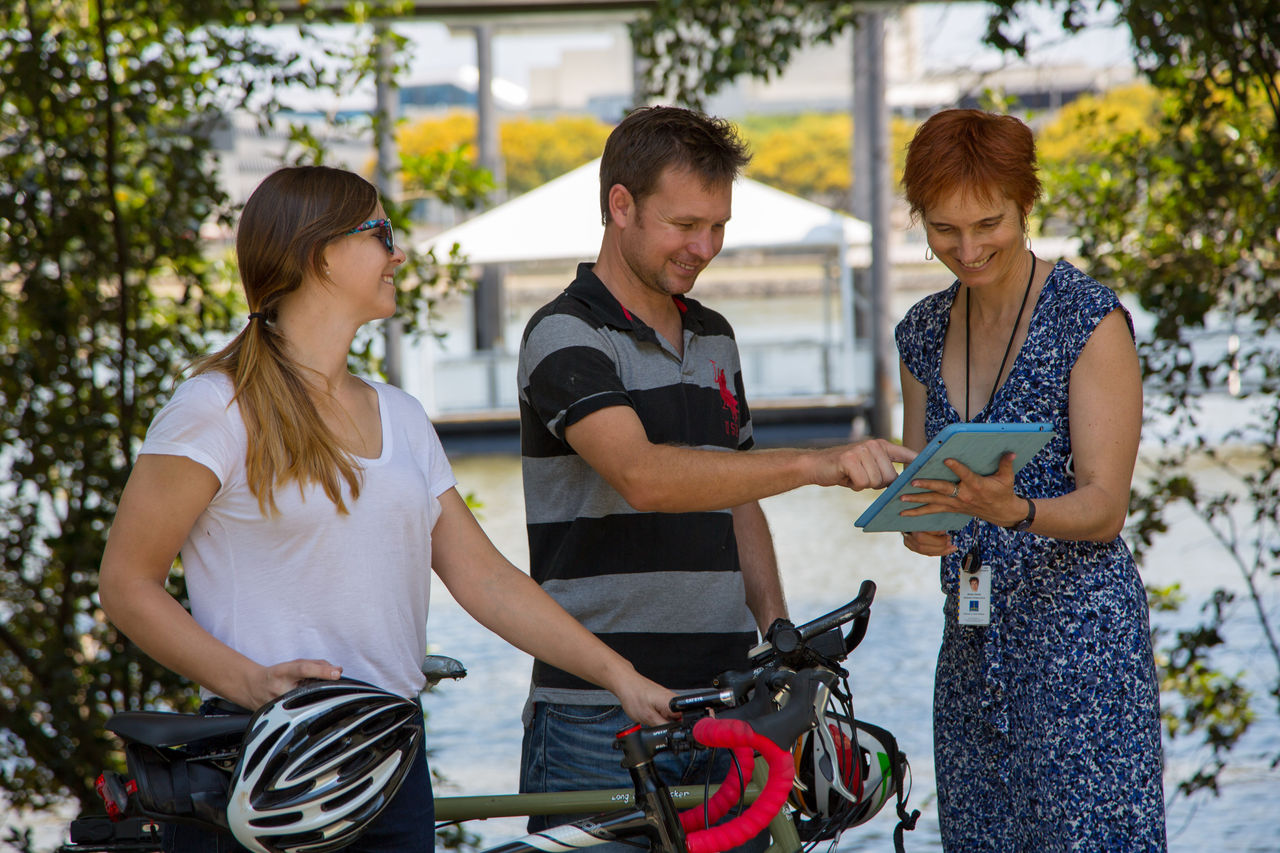 People doing an online Council survey on a tablet with a Council officer along the Brisbane River.