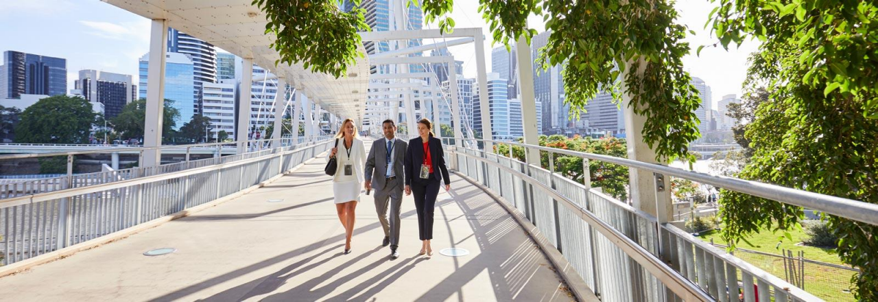Three business people walking on bridge in central business district of Brisbane.