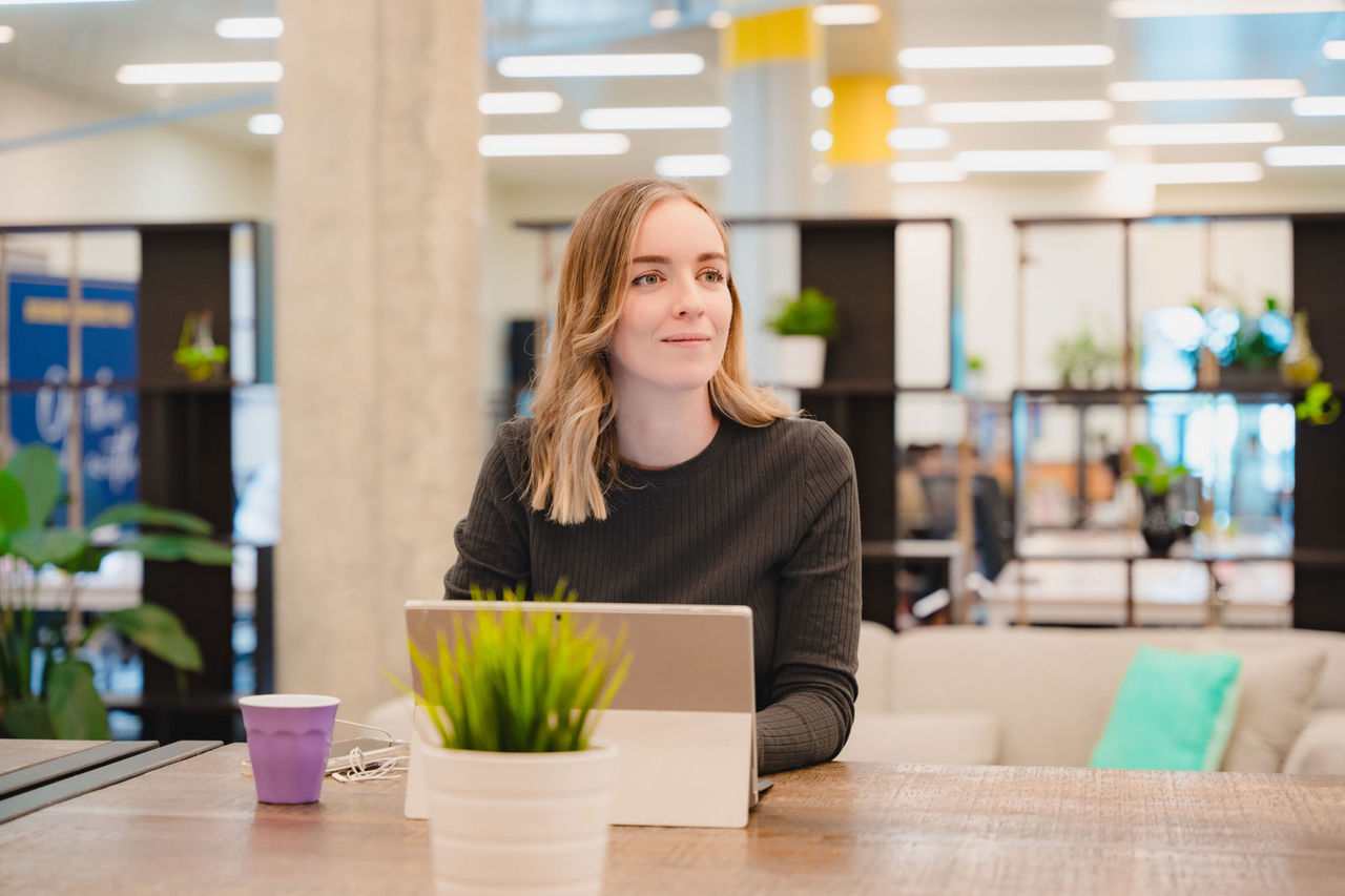Woman in front of a laptop in an open plan office environment.