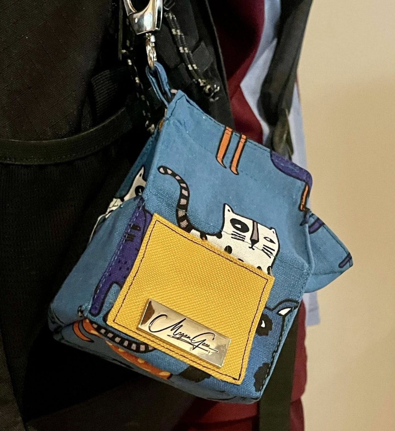 This image shows a blue and yellow handbag that features a black and white cat.