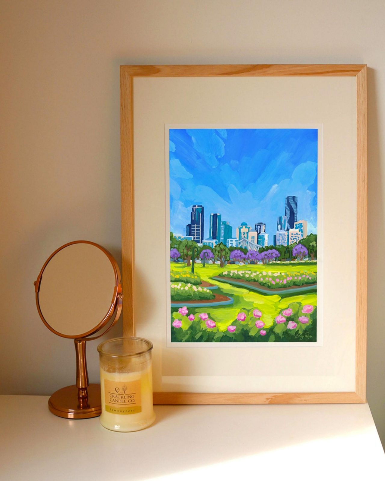 An bench with a framed artwork of a cityscape, a mirror and candle.