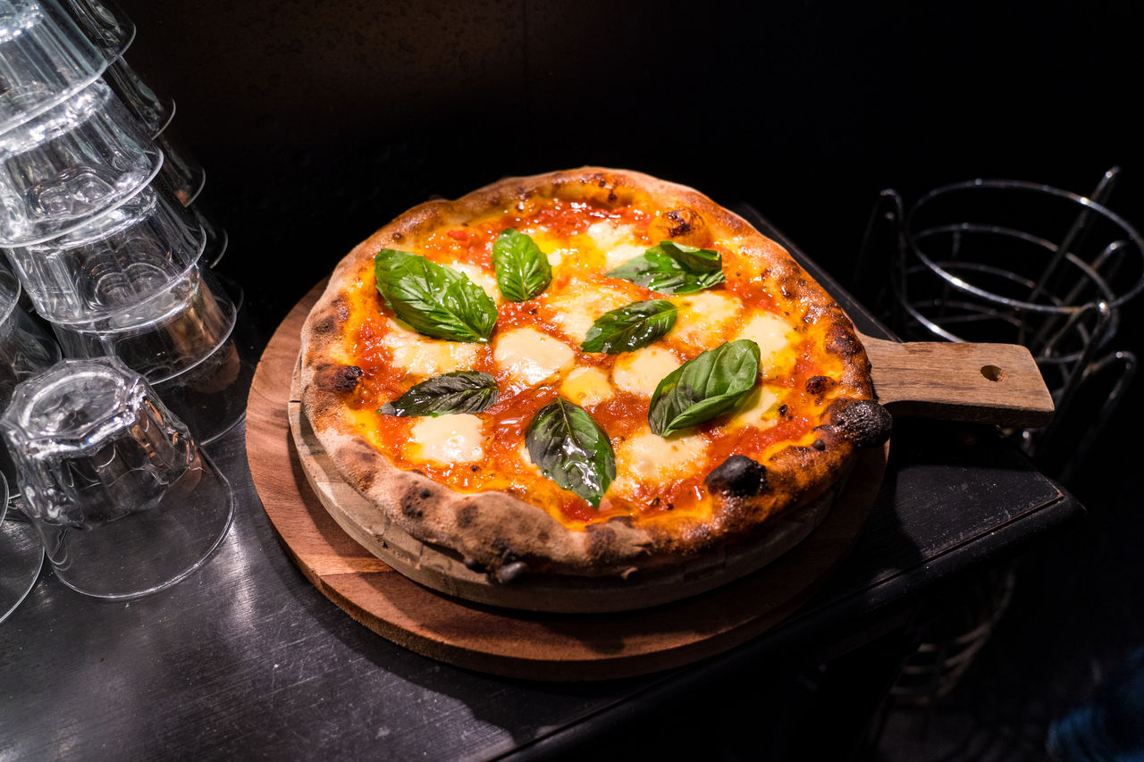 Woodfire margherita pizza on a round board with glasses to the left.