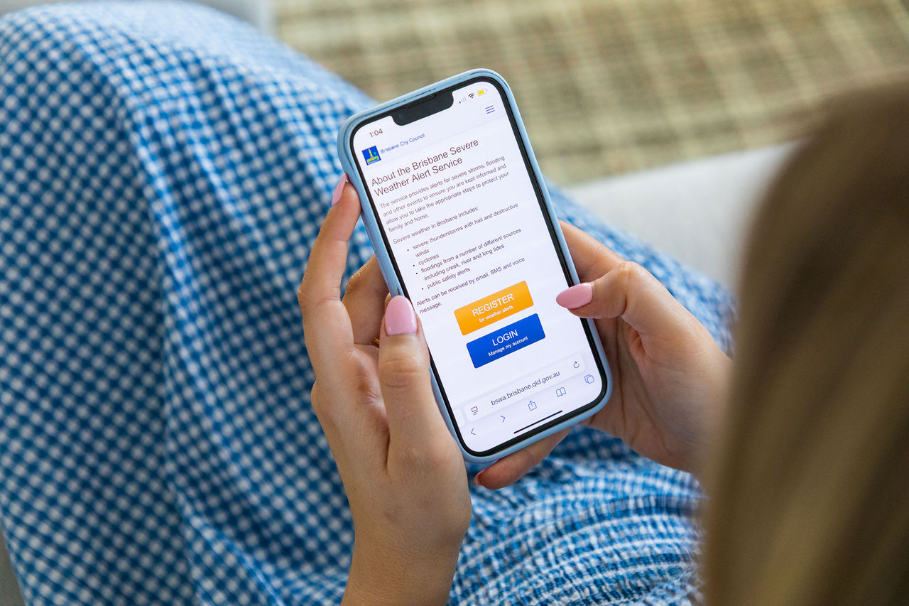 Woman looking at Brisbane Severe Weather Alert (BSWA) app on iPhone.