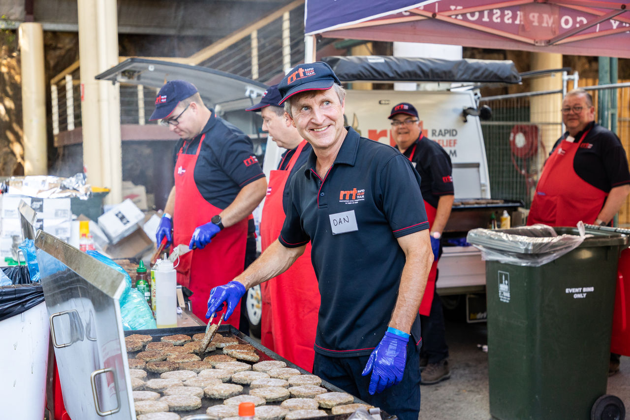 5 Male volunteers from Rapid Relief Team cooking a barbecue for guests at a 2023 Homeless Connect event.