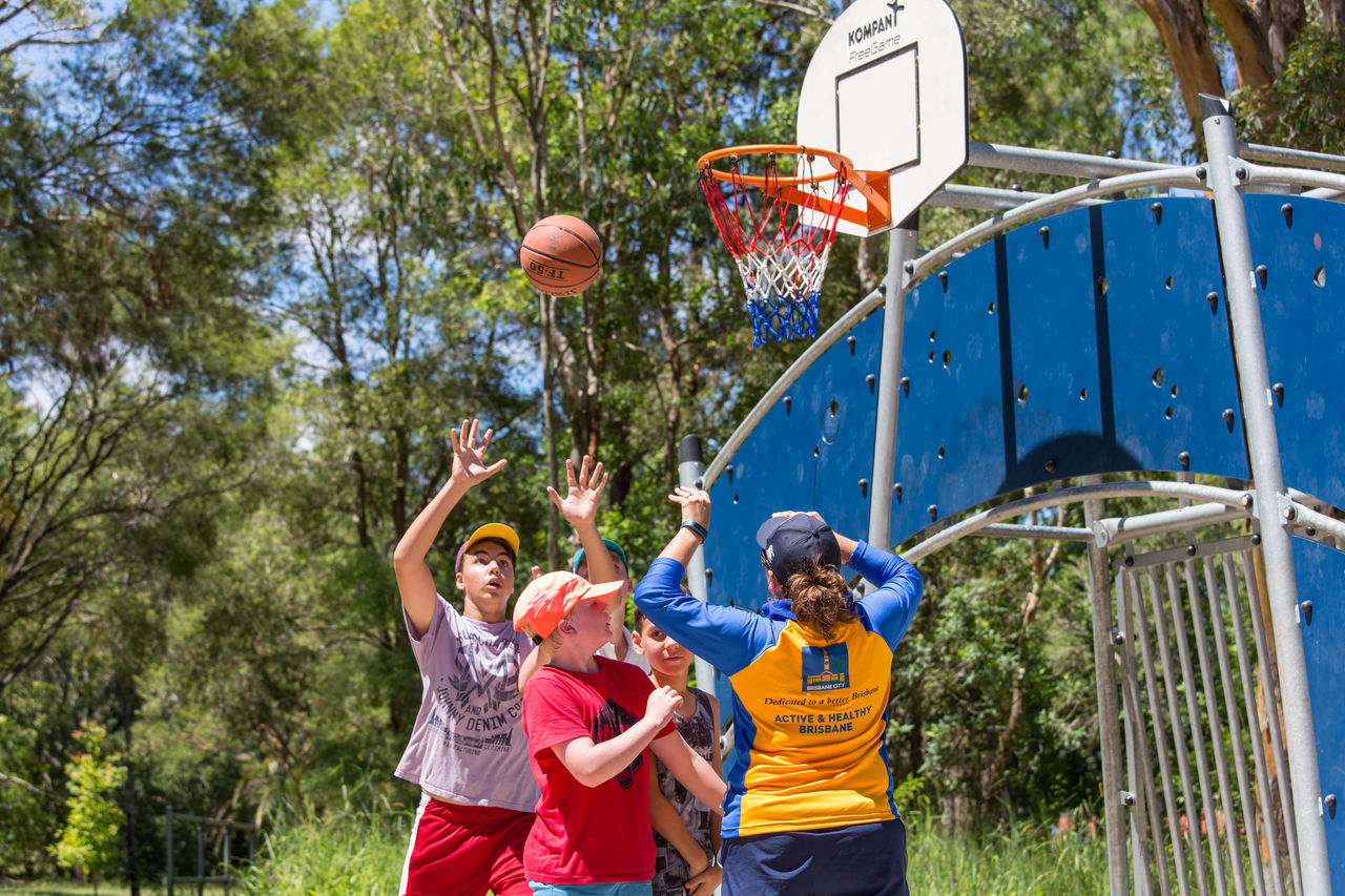 4 boys shooting hoops on a half basketball court with a female Active and Healthy event provider.