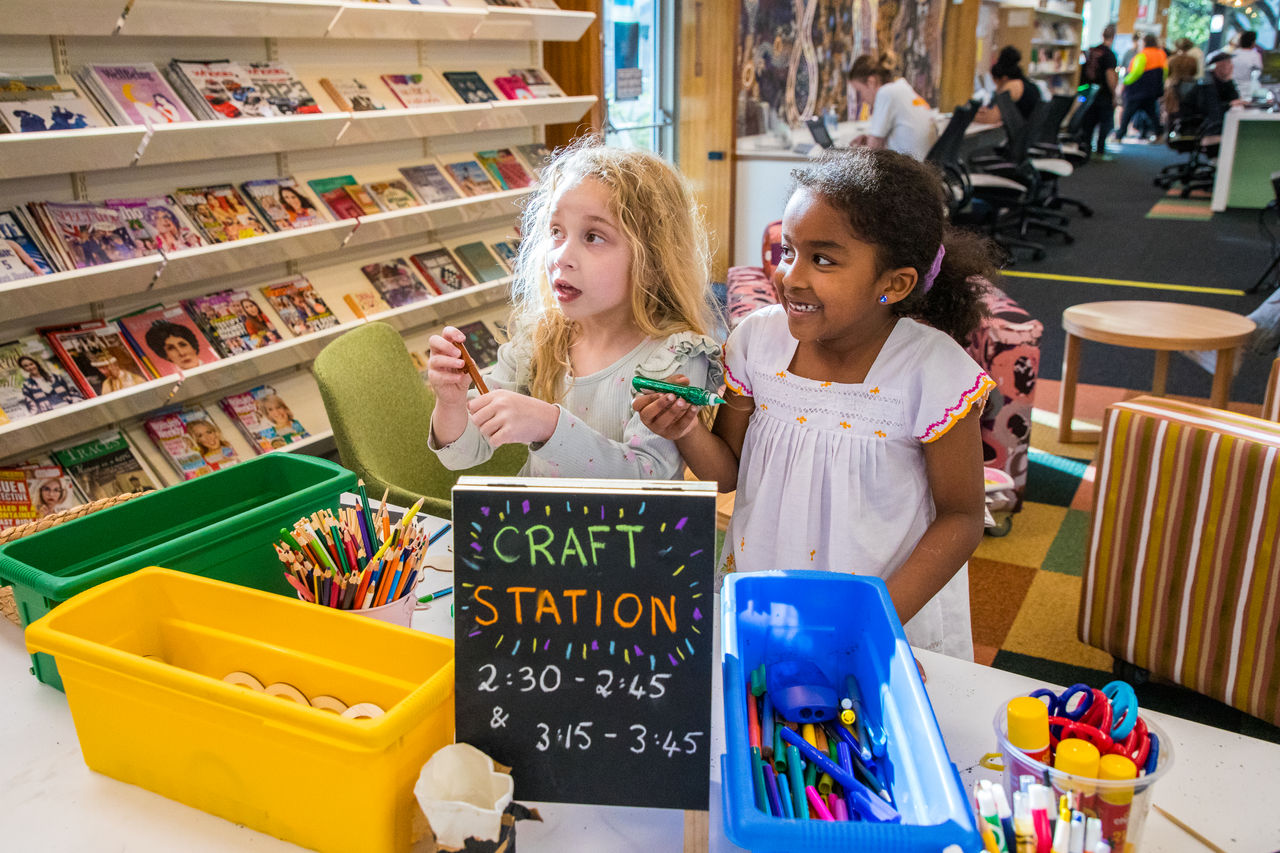 2 young girls holding pens at a craft station in Zillmere Library.