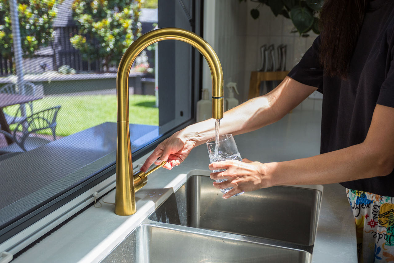 Close-up of side mid-section of woman filling up a glass at a kitchen water tap.