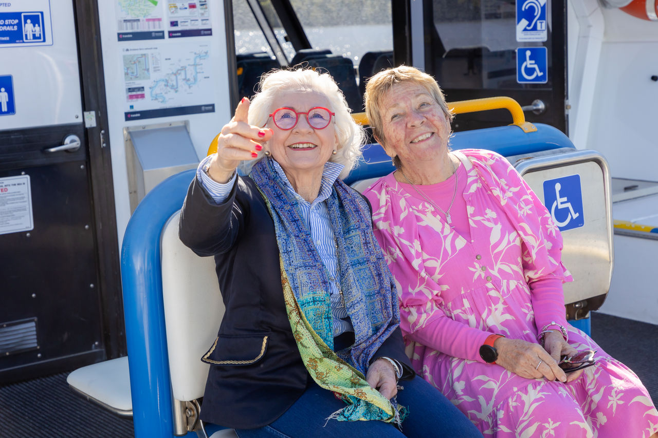 Two senior women sightseeing on the top deck of a double-decker CityCat.
