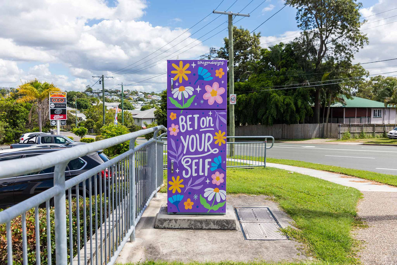 A colourful Artforce artwork on a traffic signal box with a purple background, floral design and the words 'Bet on your self'.