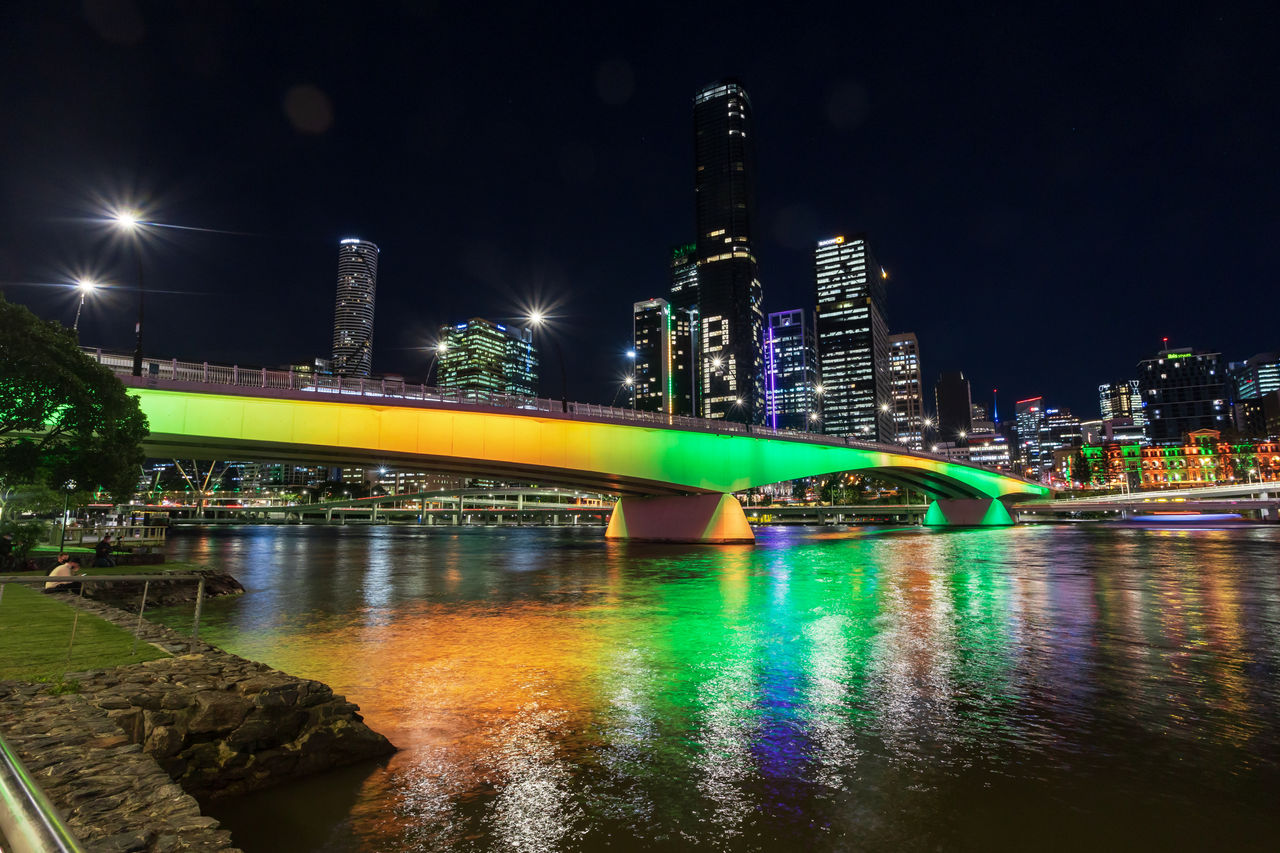 Victoria Bridge (viewed from South Bank Parklands) lit up in green and gold on sub-structure. Brisbane CBD at night in background.