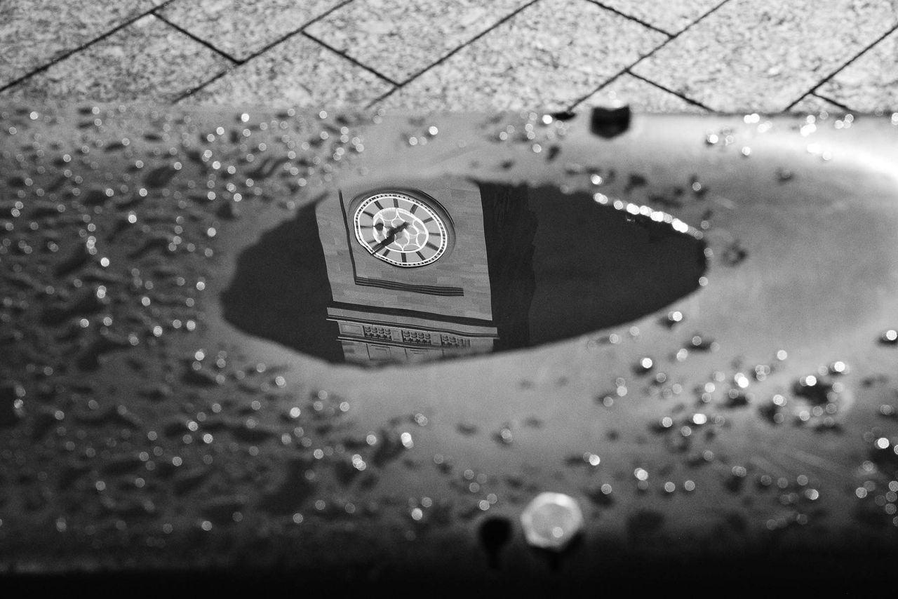 A reflection of the Brisbane City Hall Clock Tower clock in a puddle in King George Square.