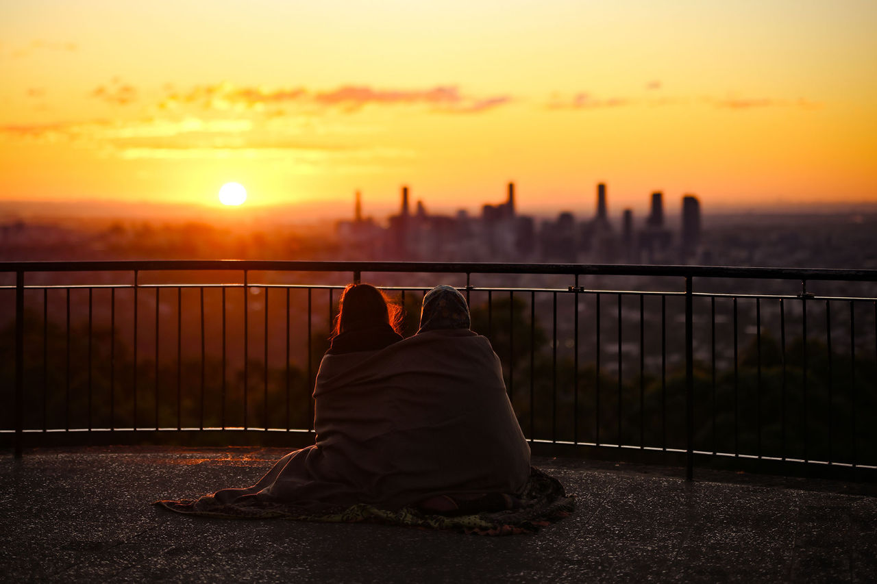 A couple sitting at Mt Coot-tha Summit at sunrise.