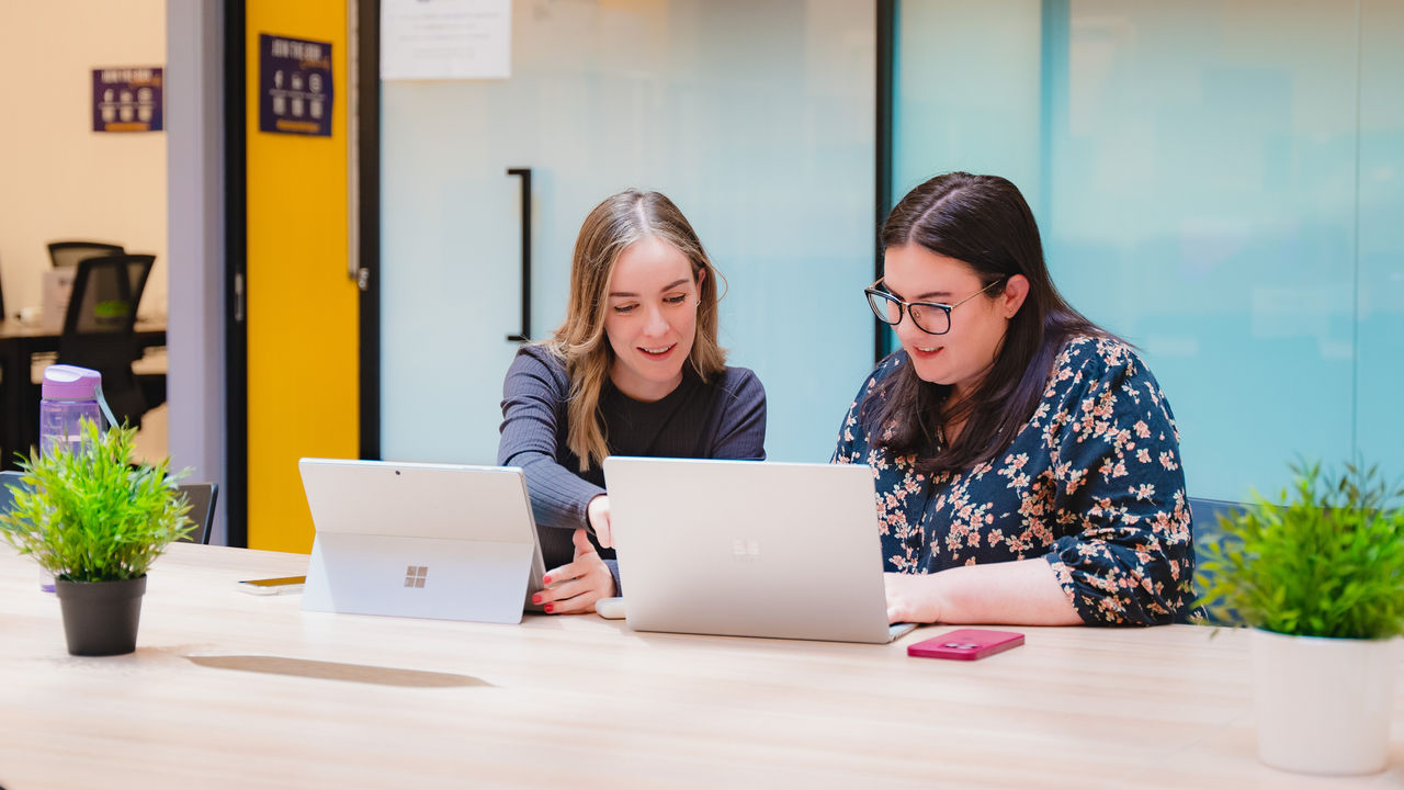 2 women working in front of laptops in an open office setting.