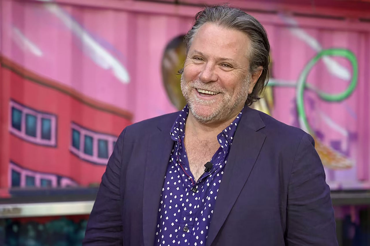 John Collins - mentor for The QUBE Effect 2026 - photographed in front of a bright-coloured mural wall.