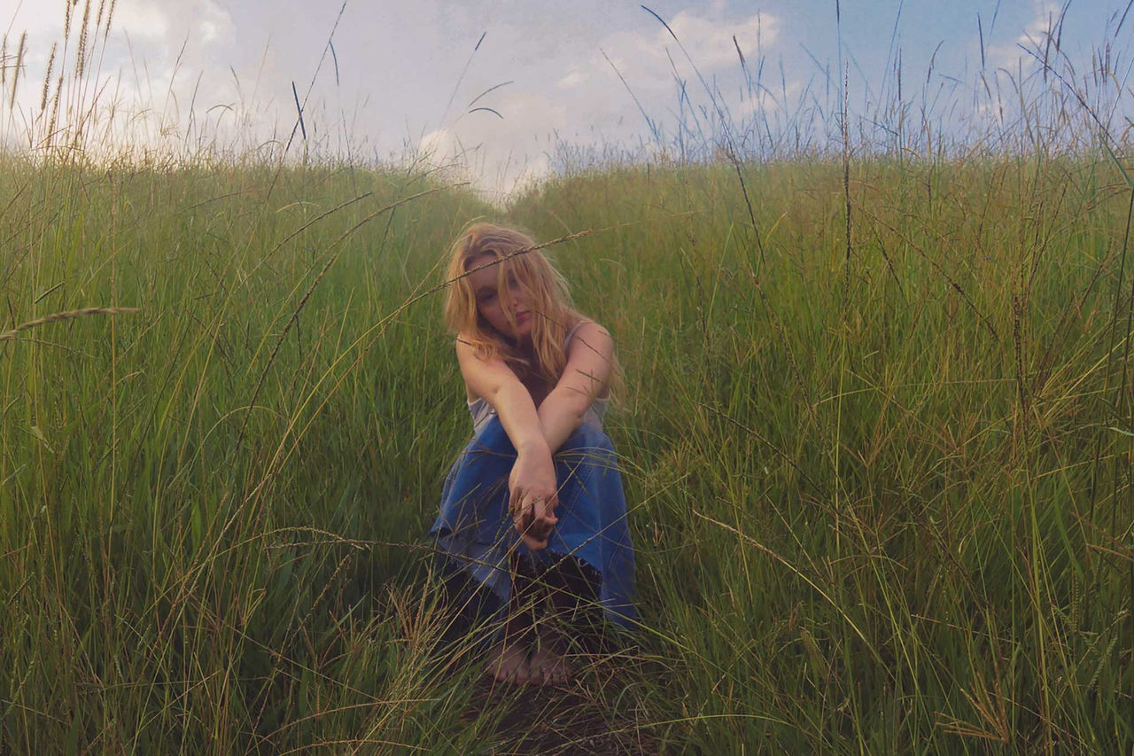 Sarah Hamze -finalist in The QUBE Effect 2026 - photographed in a field with long green grass and a blue clouded sky.