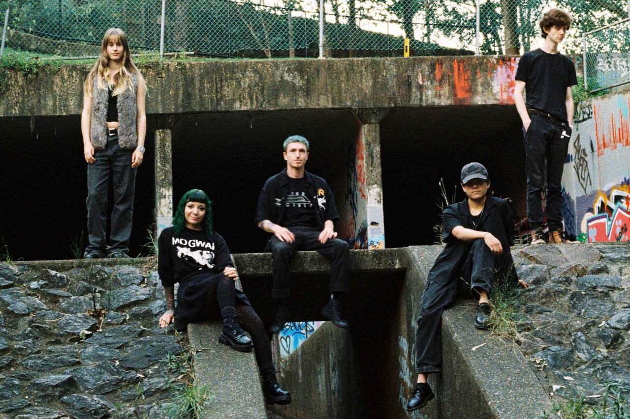 Liasis band members - finalists in The QUBE Effect 2026 - photographed at a city stormwater drain.