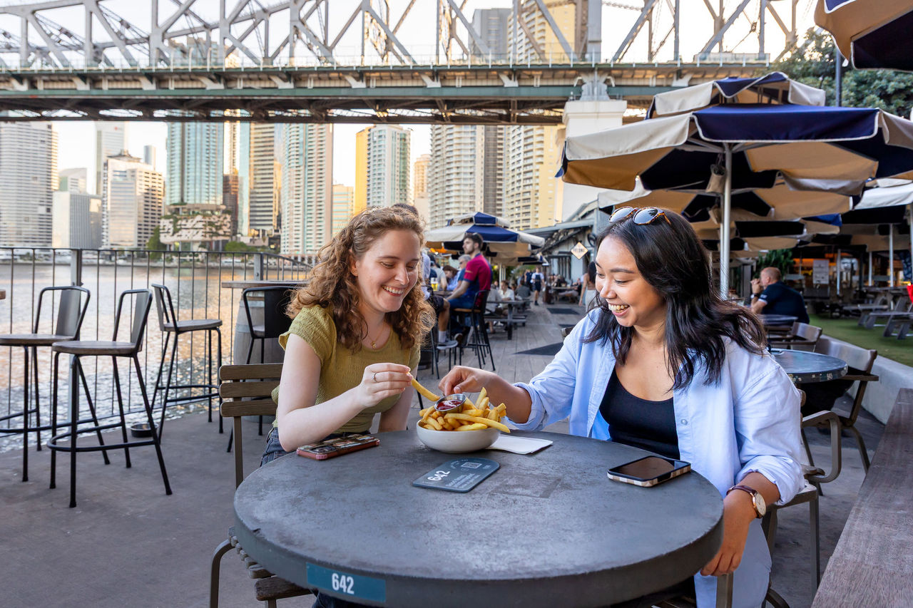 Two women sharing a bowl of hot chips at Felons, Howard Smith Wharves.