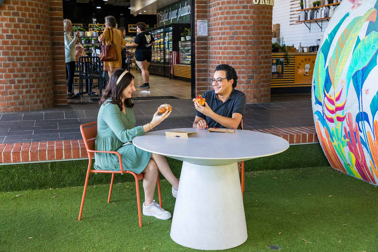 A couple sitting at a white, round table at South City Square Woolloongabba eating sweet treats.