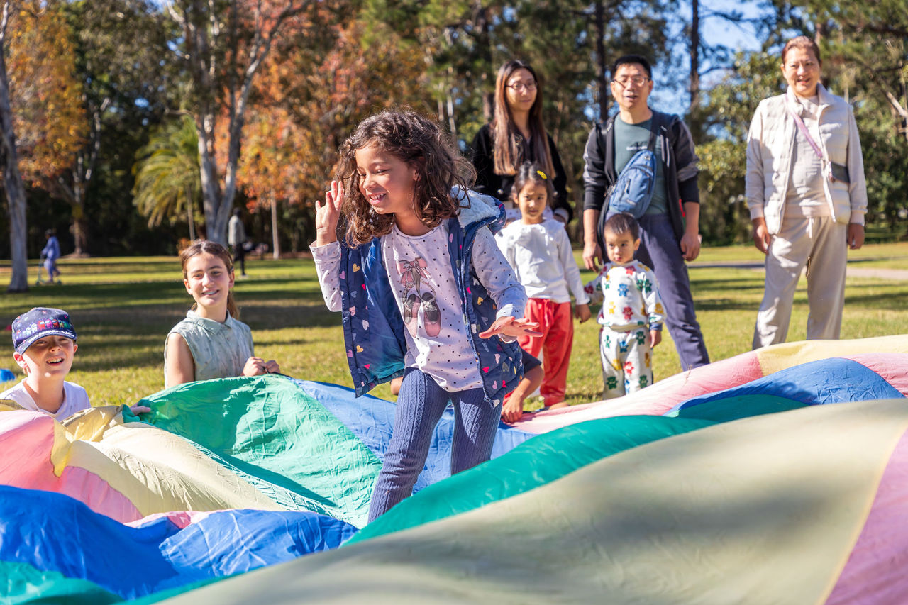 Group of kids playing with parachute mat in an Adventure Games session at Calamvale District Park.
